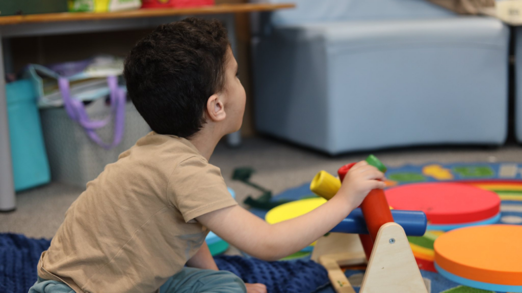 This picture shows a child sat on a carpet playing with sensory toys.