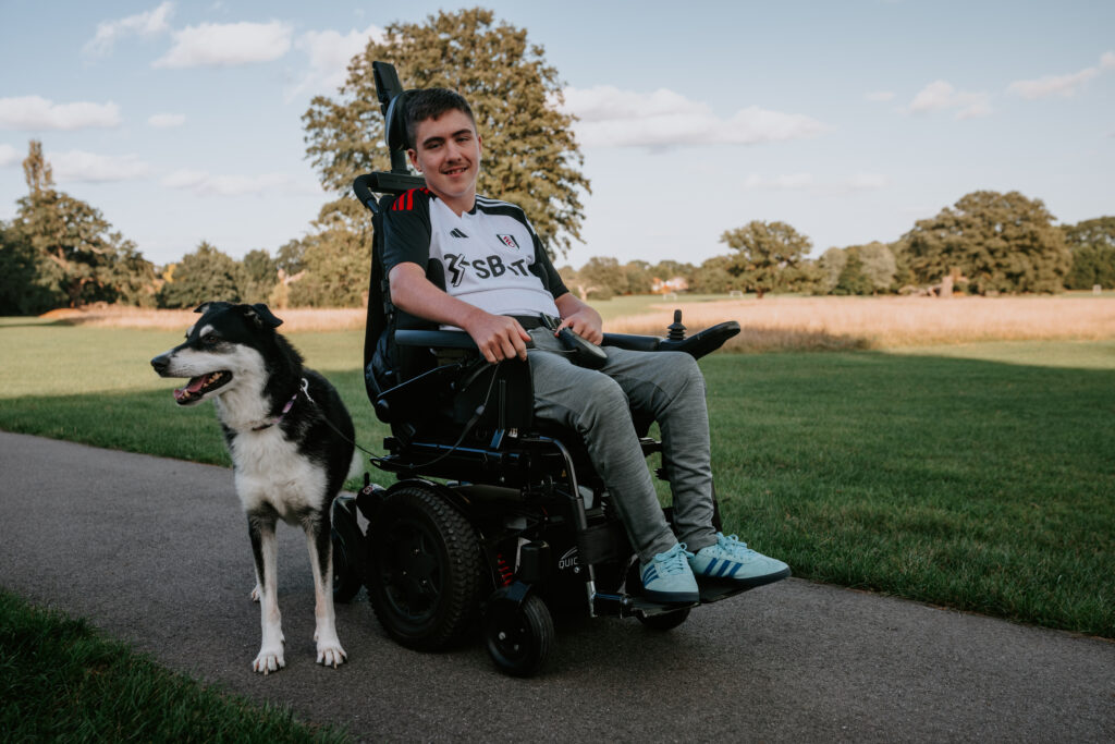 boy in an electric wheelchair with his black and white dog beside him