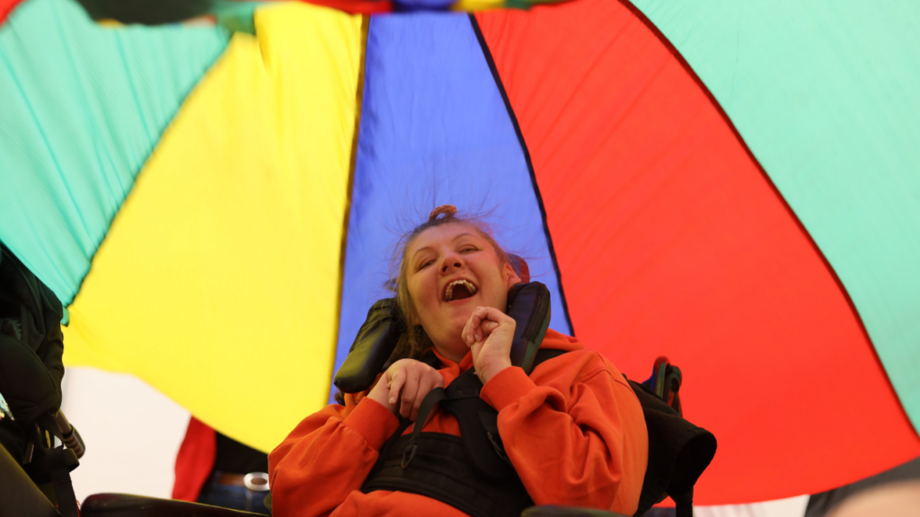 This picture shows a laughing child in a wheelchair underneath a colourful parasol.