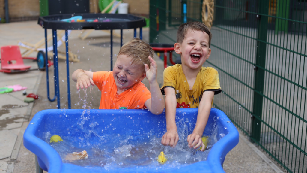 Picture shows two young children splashing on a wet play table at a childcare setting with Newlife charity