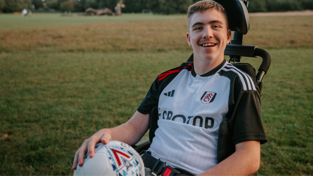 This picture shows a teenage boy in a wheelchair holding a football.