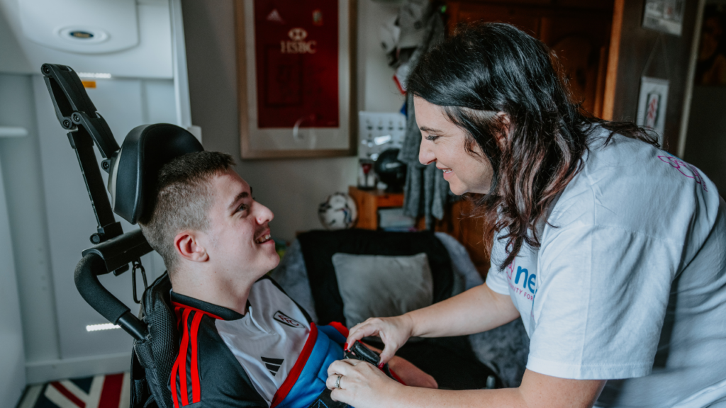 Image shows a young boy with his mum strapping him into an adapted wheelchair