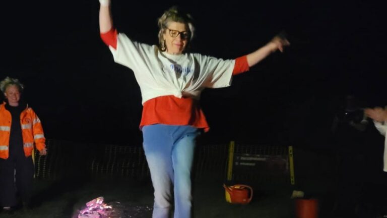 Picture shows a female walking across a firewalk with her arms raised out.