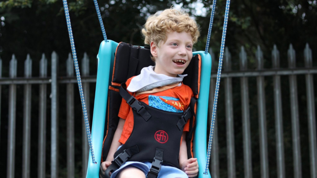 Picture shows a child using an adapted swing in a playpark.