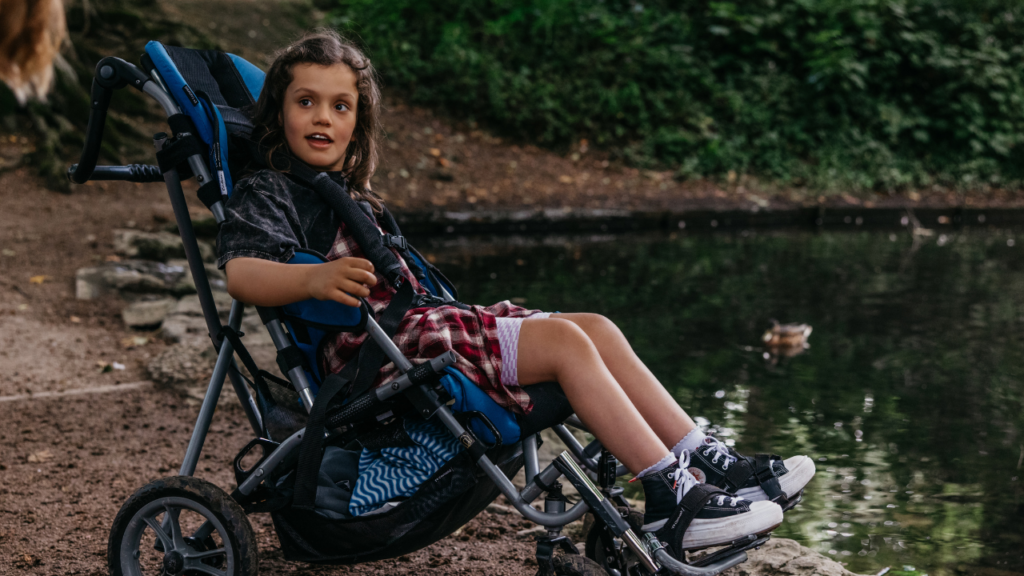 Image shows child in an adapted buggy by a lake